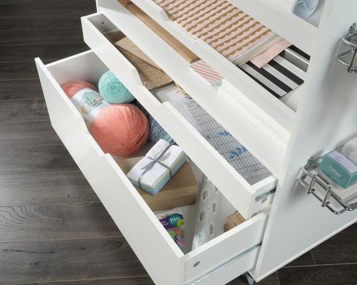 29259TK | The Teknik Office Craft Cart in a White Finish is the delightfully simple office furniture offering ideal for any office or room in the house. The generous work surface provides ample space for all of your crafting activities and it also slides out, revealing hidden divided storage for all miscellany of items. It has two height adjustable shelves which can be set at an inclined angle for easy access to craft paper. The two storage drawers with metal runners and the storage on the back of the cart is perfect for wrapping paper or fabrics. There are also metal baskets conveniently on the side of the cart to store or dispense ribbon or tape, what ever you need it for! The easy roll castors make it easy to move the cart where you need it.