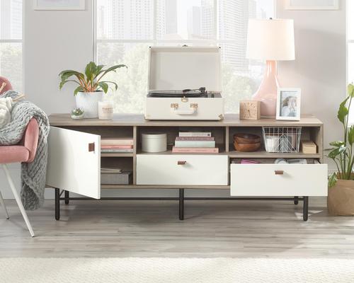 5422051 | The Teknik Office Avon Leather TV Stand/Credenza is a charming and delightful option for all office and home colour schemes.  Beautifully finished in Sky Oak with White accents, this TV /Credenza can accommodate a TV weighing a maximum of 31kg. It has an adjustable shelf which is discreetly hidden behind door for neat organisation while the two easy-glide drawers with full extension slides offer perfect storage space for smaller items, the contrasting leather handles complete the neat look. It also has two open cubbies for additional display items. Sitting on a durable powder coated metal frame, you can be ensured of greater stability which the enclosed back with pass-through opening provides discreet cable management. A wonderful versatile option for any living space. 