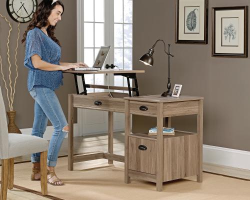 12886TK | The Teknik Office Sit Stand Desk in a charming neutral coloured Salt Oak finish is an ideal fit which will complement all home office colour schemes.  This fresh and modern styled desk benefits from a large working surface in which provides ample space for writing and computer work. The left side of the desk top lifts up and forward to create a versatile option for those that prefer to stand at their desk, which in turn will increase productivity!  Other features of this desk include hidden storage beneath the desktop, an open shelf for easy access storage, two storage drawers (the lower drawer features full extension slides to hold letter-size hanging files), and a cord management system to keep everything neat and tidy. Finished on all sides, this adaptable sit/stand desk is the perfect option for any room in your home.