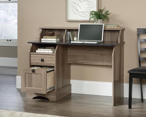 12879TK | The Teknik Office Farmhouse Desk in a Salt Oak finish with Rosso Slate accents is a classical and traditional style which will appeal to all types of home and work office environments. The Rosso Slate contrasting desktop provides ample space for writing and computer work as well as enjoying the benefits from an EverSheen top-coat which provides a clear, durable finish that resists heat, stains and scratches. There are two storage drawers featuring the patented T-lock assembly system, the lower drawer has full extension slides and holds letter-size hanging files. It also has contrasting black metal handles and three cubbys for additional storage of all your office essentials. This desk also benefits from a 360 degree finish, with the option to be freestanding.